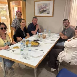Seis personas sentadas comiendo paella en un comedor con ambiente informal.