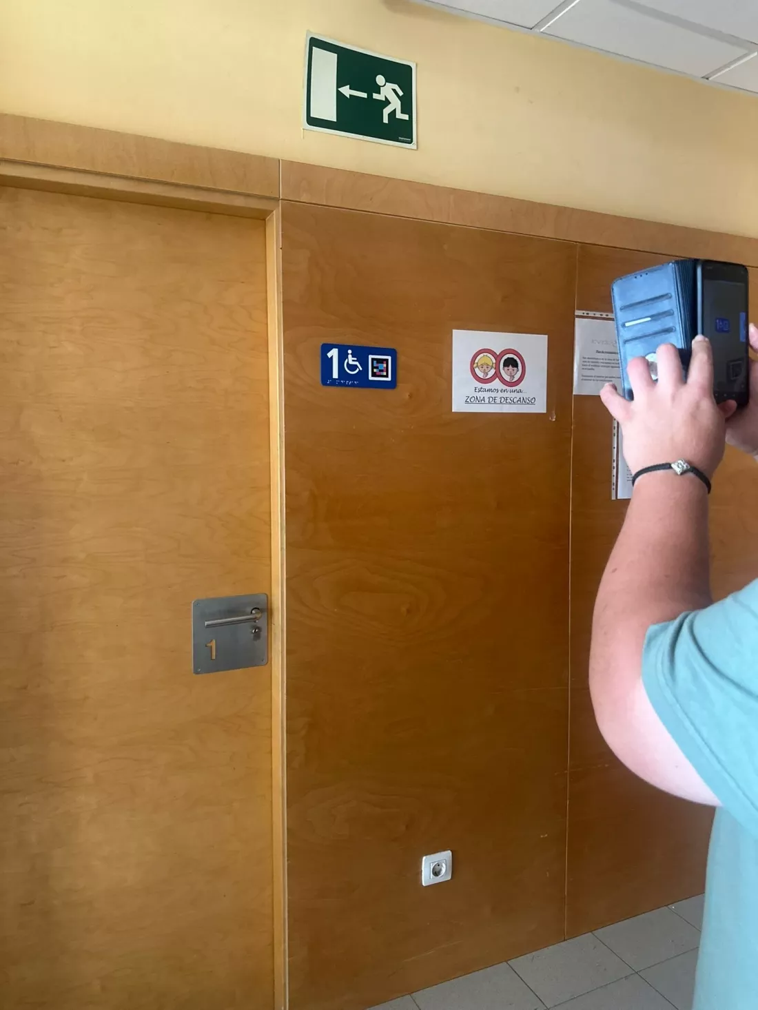 Persona usa el móvil para identificar una señal con pictograma accesible en una puerta.