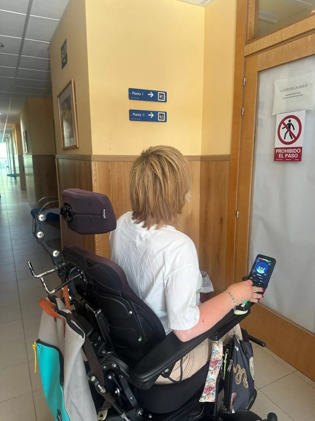 Mujer en silla de ruedas frente a señalización accesible en un pasillo.