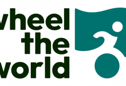 El logotipo de Wheel the World muestra el nombre de la plataforma en letras negras ("wheel the world") junto a un icono verde que representa a una persona en silla de ruedas, simbolizando el compromiso con el turismo accesible para todas las personas.