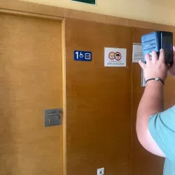 Persona usa el móvil para identificar una señal con pictograma accesible en una puerta.