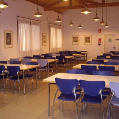 Amplio comedor junto a la cocina con mesas rectangulares y varias sillas