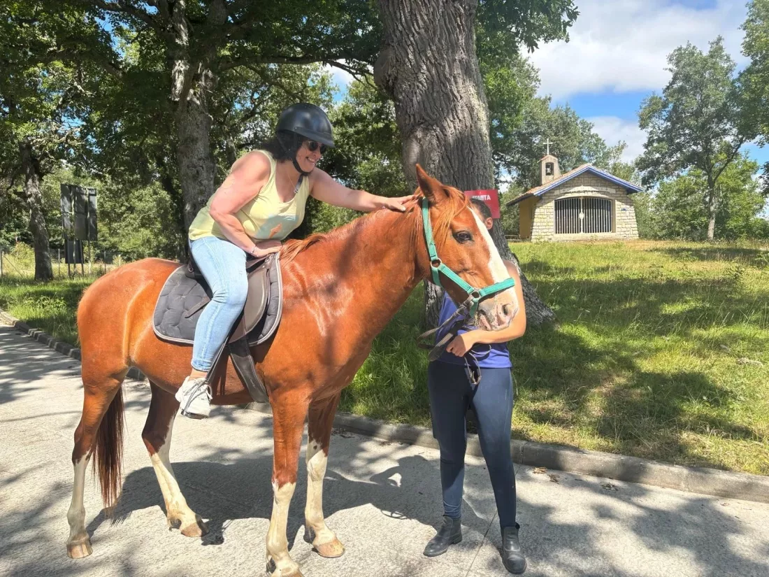 Mujer montada en un caballo frente a una pequeña ermita