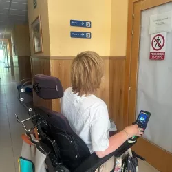 Mujer en silla de ruedas frente a señalización accesible en un pasillo.