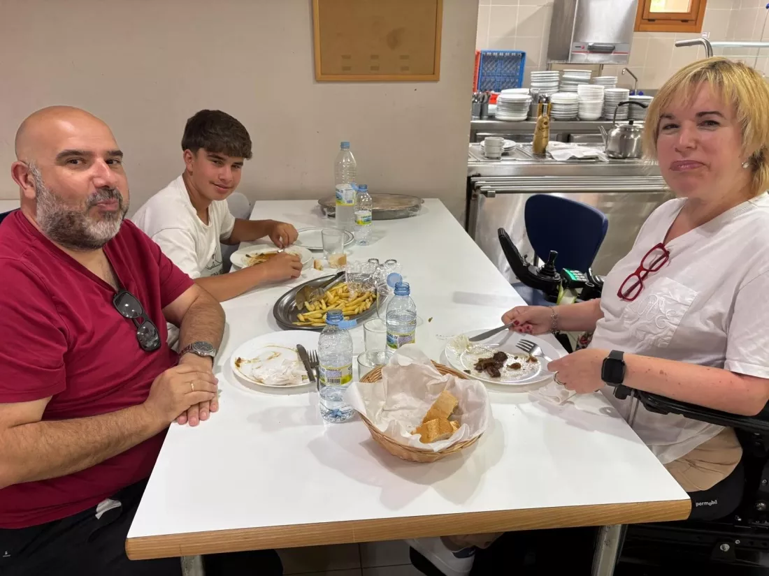 Tres personas comiendo en un comedor, una de ellas en silla de ruedas.