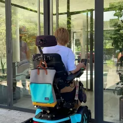 Mujer en silla de ruedas frente a la entrada principal de un edificio.