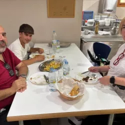Tres personas comiendo en un comedor, una de ellas en silla de ruedas.