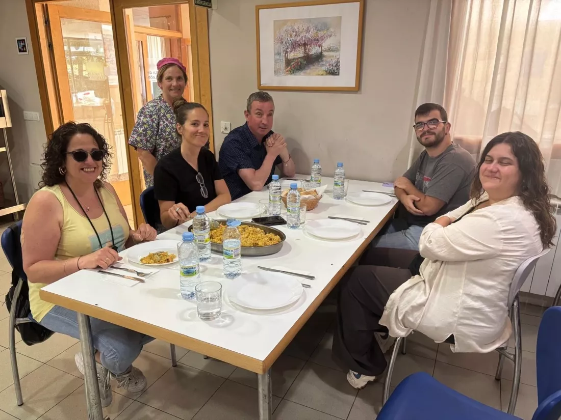 Seis personas sentadas comiendo paella en un comedor con ambiente informal.