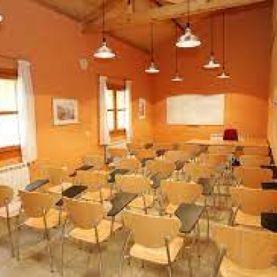 Aula más grande con sillas de madera y pantalla de proyección