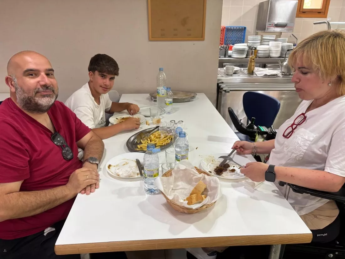 Tres personas sentadas comiendo, una de ellas en silla de ruedas, en un comedor accesible.