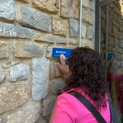 Mujer toca una señal en braille que indica "Rocódromo" en una pared de piedra.