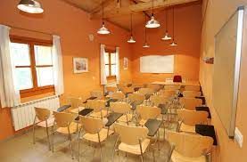 Aula más grande con sillas de madera y pantalla de proyección